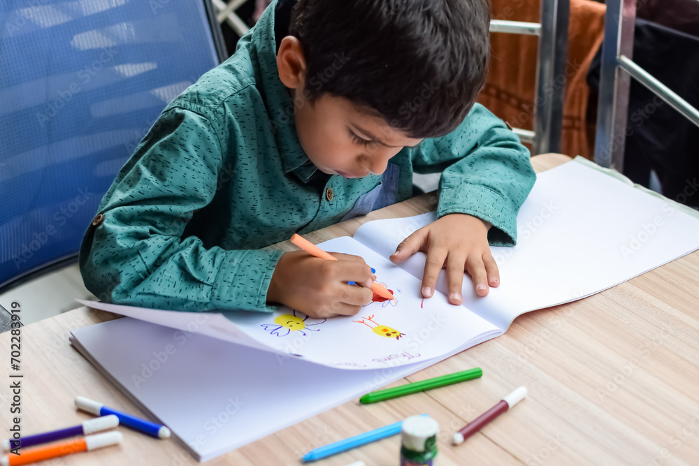 Smart Indian little boy perform thumb painting with different colourful water colour kit during the summer vacations, Cute Indian Kid doing colourful thumb painting drawing on wooden table Smart Indian little boy perform thumb painting with different colourful water colour kit during the summer vacations, Cute Indian Kid doing colourful thumb painting drawing on wooden table