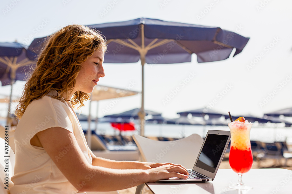 Woman using laptop to check email for work and using laptop computer on beach