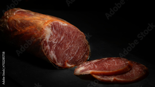 Lomo ibérico. Iberian loin from Spain on a black background prepared to eat. Iberian bait loin sausage stuffed and cured in the cellar. Delicious cured Iberian pork loin. Copy space photo