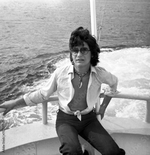 Photo from an old black and white negative of a male teenager sitting on a motorboat stern. A self-portrait.