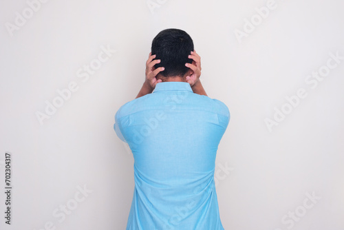 Back view of a man showing scared expression with both hands covering his ears photo