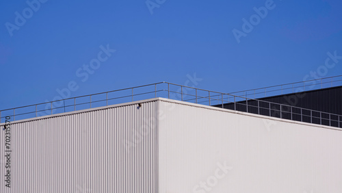 Modern white and black aluminium corrugated factory buildings with steel fence on rooftop against blue clear sky background