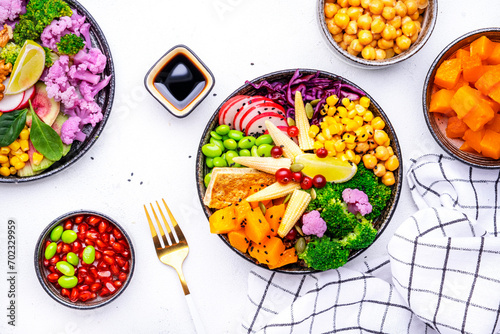Vegan buddha bowl with sweet potato, quinoa, chickpeas, soybeans edamame, tofu, corn, cabbage, radish, broccoli and seeds, white table background, top view. Healthy vegetarian comfort food