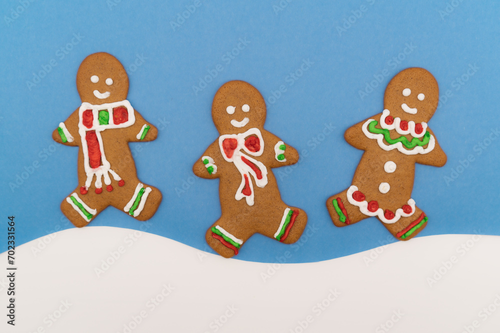 Three colorful gingerbread men cookies on a blue and white snow background 
