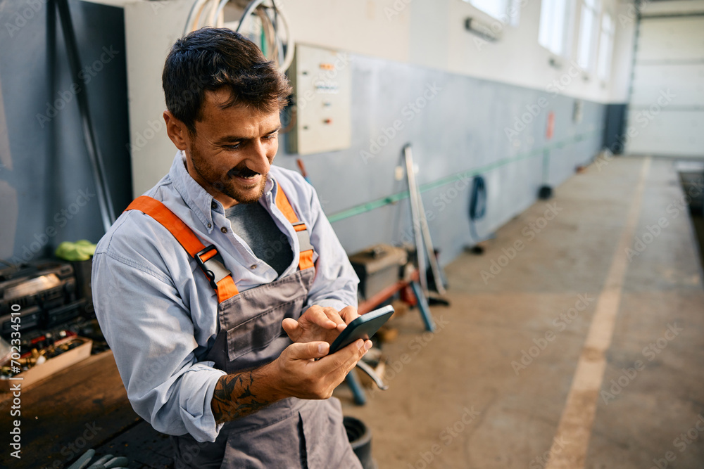 Happy mechanic texting on cell phone while working in garage. Happy mechanic texting on cell phone while working in garage.
