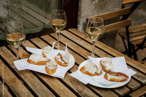 Venice, Italy, 12 February 2023: Cichetti Venetian tapas with cod mash, cafe restaurant Bacari, Traditional Appetizers snacks accompanied with three glass of white wine, bar food, wooden table