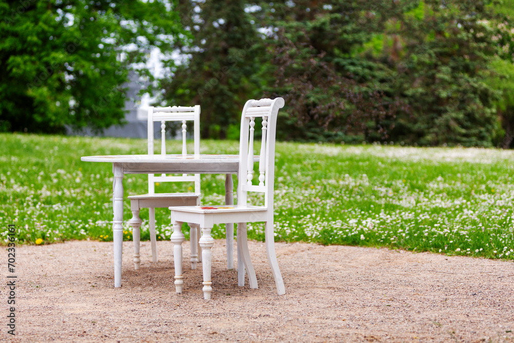 White table and two white chairs on a green lawn. Summer day outdoor