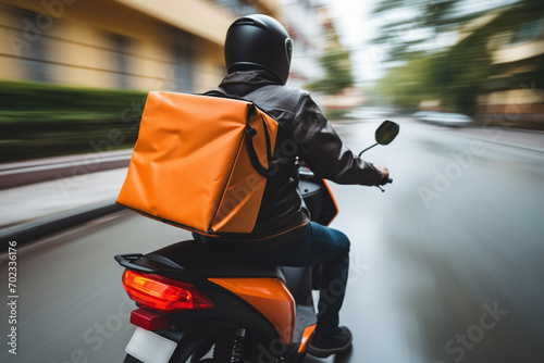 delivery man with orange rectangular backpack on moped, back view, blurred backgroundsdelivery man with orange rectangular backpack on moped, back view, blurred backgrounds