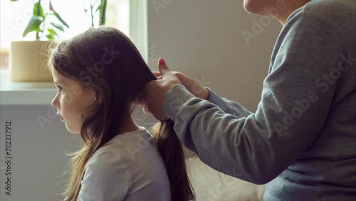 Mom combs her beloved daughter's long hair with massage comb in morning at window of house. Timelapse. Mothers and daughters. Hair care. Motherhood. Happy childhood. Love and care. 4k footage.