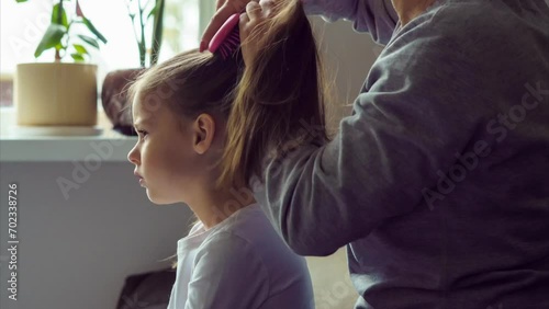 Shooting style is timelapse. Mom combs her little daughter at home and makes her two ponytails. Mothers and daughters. Hair care. Motherhood. Happy childhood. Love and care. 4k footage.