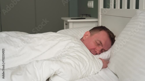 Awakening. Man wakes up from alarm clock in his phone, turns it off and tries to fall asleep again. Interior of bedroom. Natural fabrics and materials. Sleep problems. Bleachers. 4k footage.