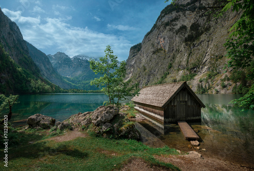 Boathouse with mountain cliffs on lake Obersee at Berchtesgaden Bavaria, clouds in blue sky, turquoise calm water, Berchtesgaden Bavaria.