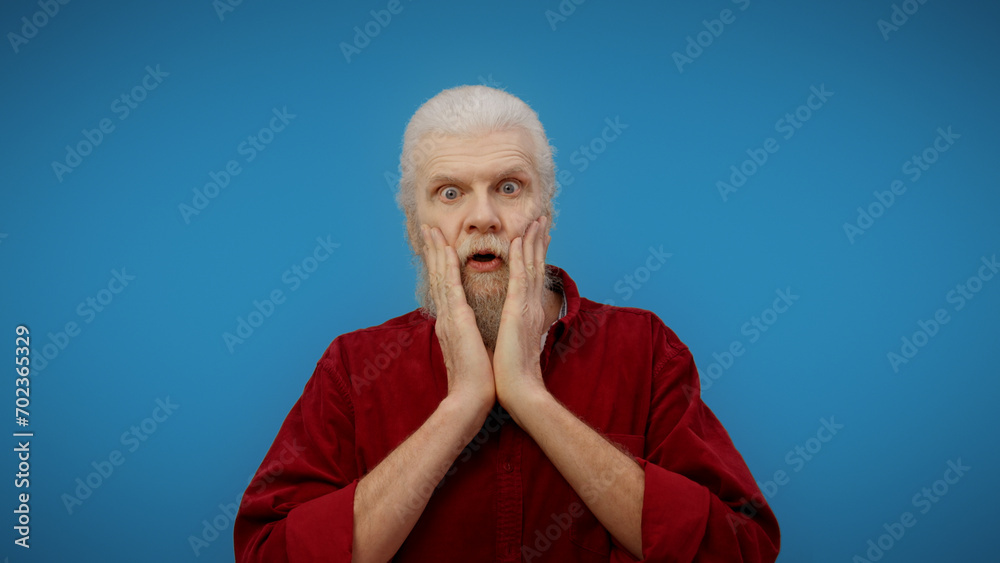 Portrait of a surprised and shocked senior man against a blue background, a picture of pure amazement