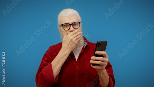 Senior man sees shocking news on his smartphone, feeling confused and disbelieving photo