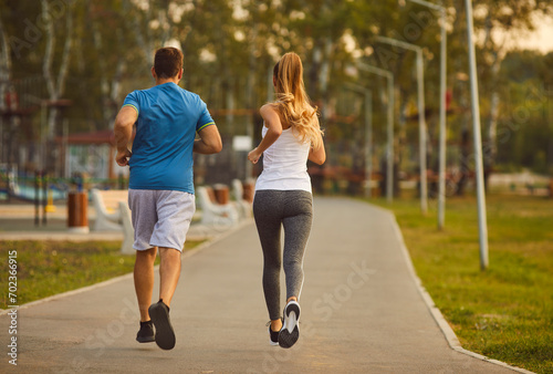 Energize your morning. Active young sports couple doing sports running together in city park in morning. Rear view of slim woman and man in sportswear jogging together in park on jogging track. photo