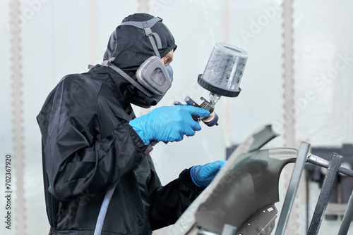 A meticulous technician ensures a flawless paint job dressed in a black jumpsuit in a professional paint chamber.