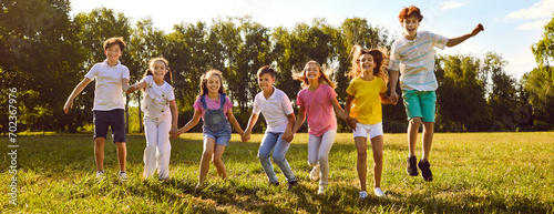 Teenage happy kids friends jumping on green grass in the summer park standing in a line. Smiling children boys and girls having fun together outdoors on a sunny day in nature. Banner.