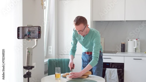 Lonely man in morning, in kitchen, he shoots breakfast on phone camera. He's making toast, there's glass of juice next to it. Modern technologies. Professions online. 4k footage.
