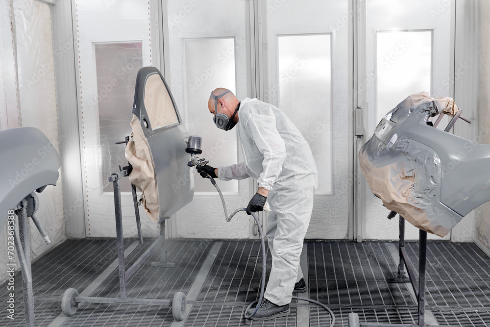 A dedicated craftsman in a respirator and overalls meticulously paints a car's components. A dedicated craftsman in a respirator and overalls meticulously paints a car's components.