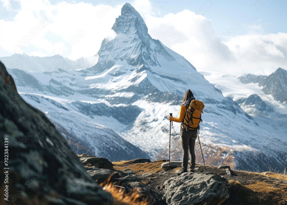 A woman trekker stands atop Matterhorn, surrounded by the unique beauty of the Alps, a testament to the majesty of nature and the thrill of alpine adventure