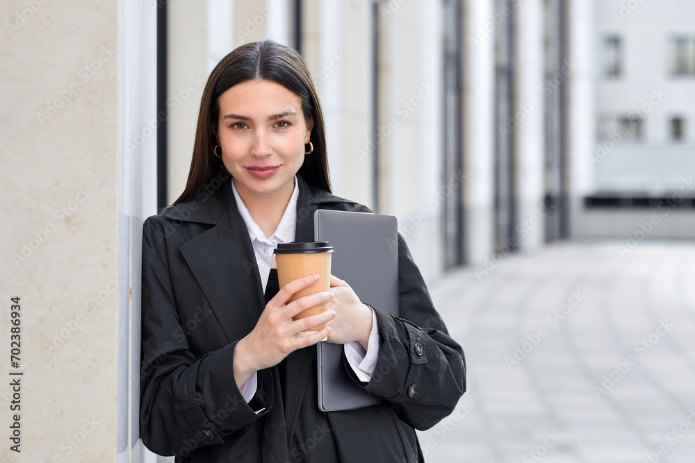 Portrait of a confident young Caucasian woman with black hair dressed in a black cloak with a laptop in her hand Portrait of a confident young Caucasian woman with black hair dressed in a black cloak with a laptop in her hand