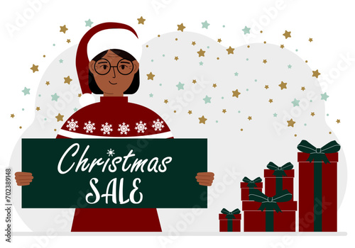 A woman in a sweater and a red Santa hat holds a poster with the text about Christmas sale in his hand.