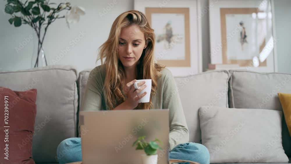 Video of beautiful young woman working with her laptop while drinking a cup of coffee sitting on a couch at home Video of beautiful young woman working with her laptop while drinking a cup of coffee sitting on a couch at home