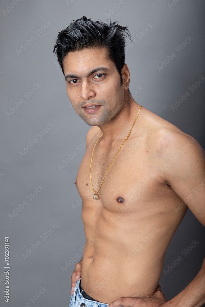 Portrait of a shirtless sensual young man. Healthy muscular man with black hair, posing in bare upper body on grey background.