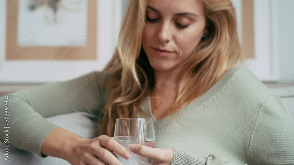 Video of unhealthy young woman with headache putting a pill in a glass of water sitting on sofa at home Video of unhealthy young woman with headache putting a pill in a glass of water sitting on sofa at home