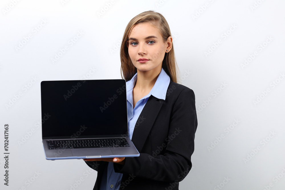 Caucasian fair-haired young woman in a business bow holds a laptop on a light background with copy space Caucasian fair-haired young woman in a business bow holds a laptop on a light background with copy space