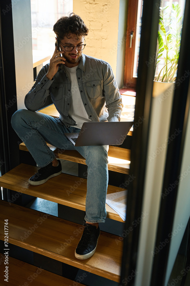 Businessman talking on smartphone and watching on laptop on stairs Businessman talking on smartphone and watching on laptop on stairs