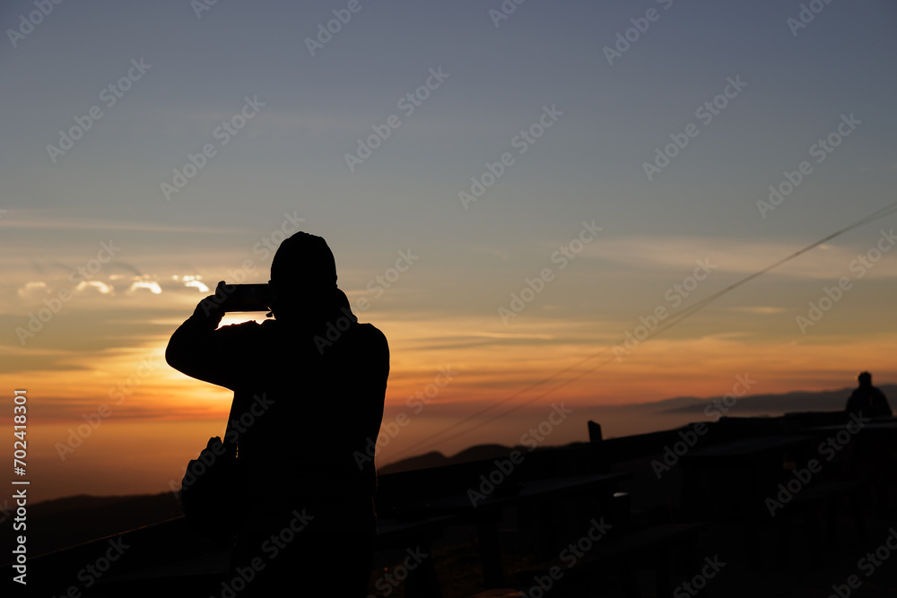 fotografando il tramonto con lo smartphone. dettagli di una persona irriconoscibile, girata di spalle e in controluce, mentre fotografa il tramonto arancione in un cielo parzialmente nuvoloso
