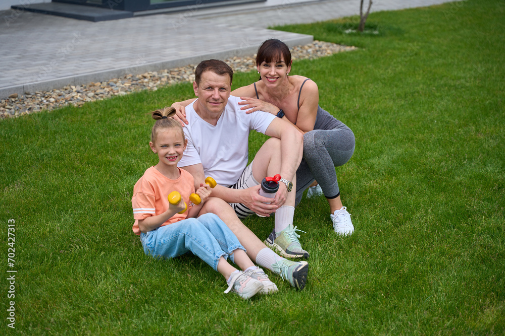 Caucasian family sitting on green grass and looking at camera in yard Caucasian family sitting on green grass and looking at camera in yard