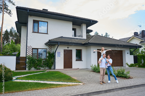 Joyful mother and daughter on father's shoulders in front of modern townhouse