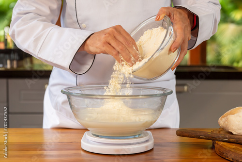 detalhe das mãos da chef de cozinha segurando em uma das mãos uma tigela de vidro com farinha de trigo e com a outra mão jogando um punhado de trigo em outra tigela preparando a receita. photo
