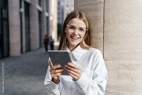 Smiling professional woman using a tablet on city streets, reflecting a tech-savvy lifestyle.