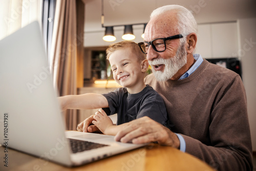 A cheerful grandfather and grandson sitting at home and smiling at the laptop. photo