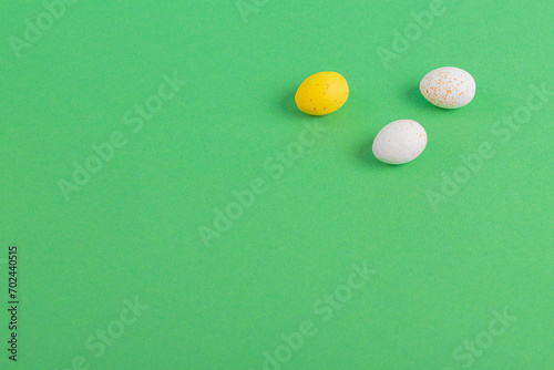 Minimalistic easter background of chocolate candy yellow and white eggs on green background. Top view with free copy space for text