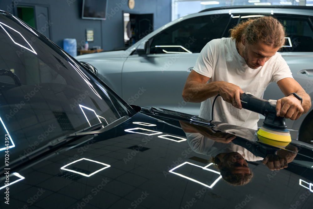 Long-haired young man polishes the body of a black car Long-haired young man polishes the body of a black car