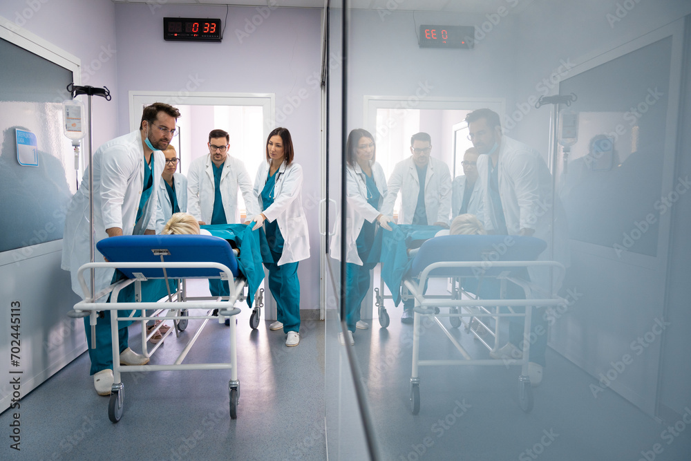 Group of male and female surgeons and doctors pushing unconscious patient on the bed into urgent surgery at hospital. Medical team in a hurry to save patients life. Group of male and female surgeons and doctors pushing unconscious patient on the bed into urgent surgery at hospital. Medical team in a hurry to save patients life.