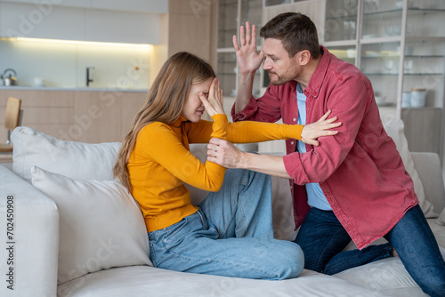 Crying woman suffering from domestic aggression, violence, protecting from tyrant man ready to hit, beat. Nervous husband, tyrant, aggressor, narcissist threatening wife. Relationship difficulties photo