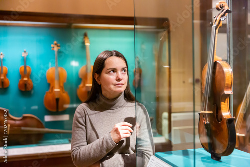 Female museum visitor examining with interest ancient stringed musical instruments displayed on exhibition .. photo