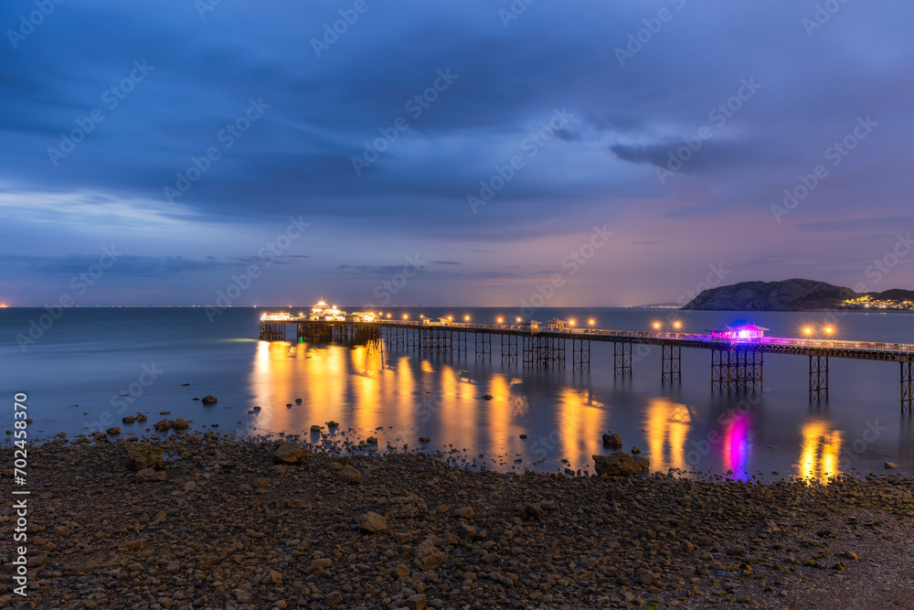 Long historic pleasure pier at dusk with lights reflecting in the water. Llandudno seaside resort, North Wales Long historic pleasure pier at dusk with lights reflecting in the water. Llandudno seaside resort, North Wales