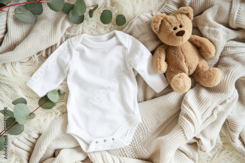 White cotton baby short sleeve bodysuit, toy teddy bear and eucalyptus branch on white ivory blanket throw background. Blank infant onesie mockup template. Top view photo