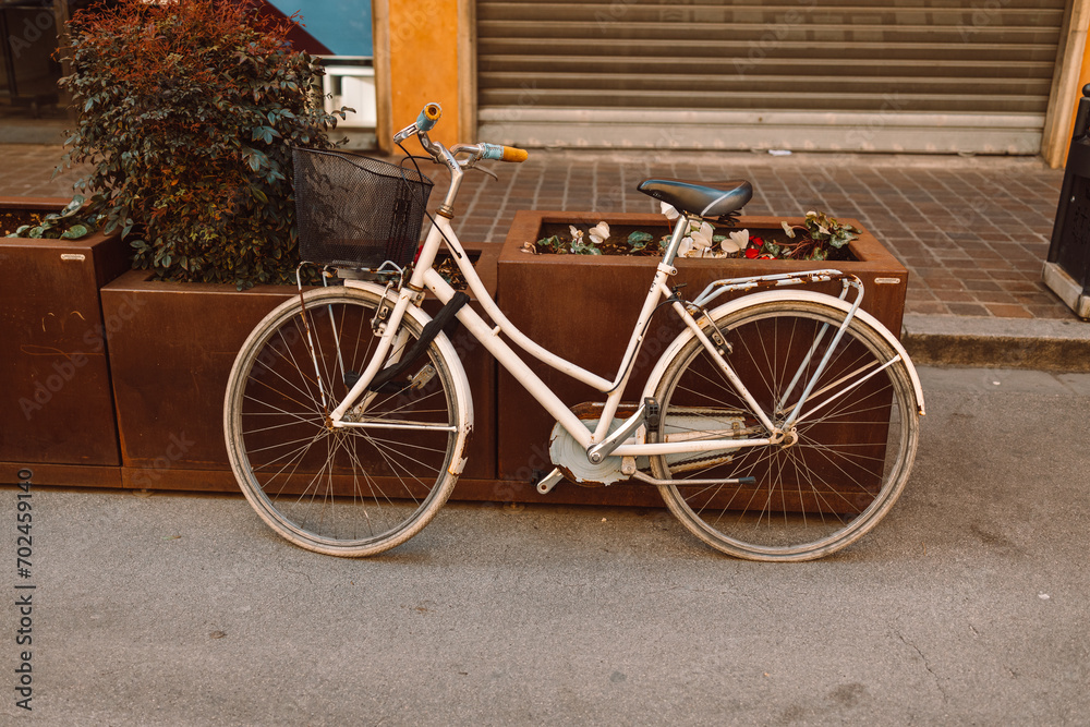 A bicycle parked on a street in Valencia, Spain. An old white bicycle near a flower bed in the center of a strictly urban area