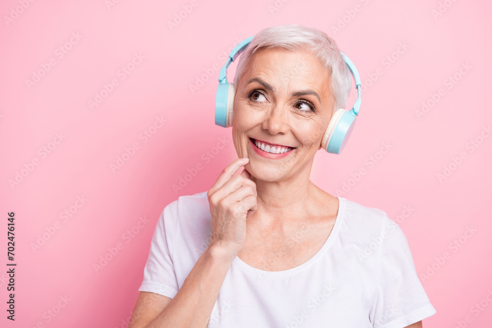 Photo portrait of lovely senior lady headphones look interested empty space wear trendy white garment isolated on pink color background Photo portrait of lovely senior lady headphones look interested empty space wear trendy white garment isolated on pink color background