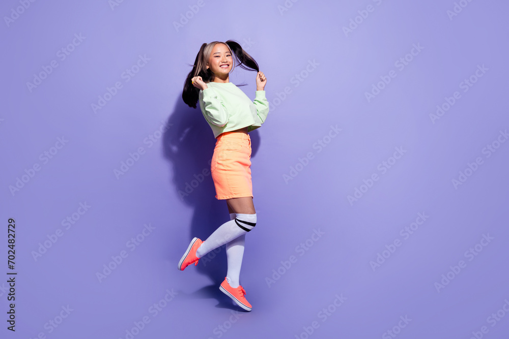 Full length photo of carefree millennial miniature girl jump air touching ponytails and have some fun isolated on purple color background