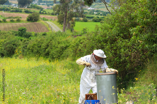 Mujer latina apicultora vestida con un traje protector blanco y esta pulsando la maquinas extractora de miel en un campo florido en las montañas de los andes