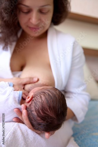 Beautiful happy loving young mother smiles while connects with her newborn baby, holds him in her arms, breastfeeds him