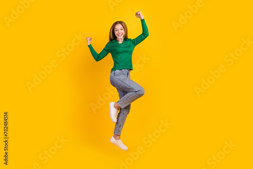Full length photo of achievement teenager girl celebrate her winnings in competition jumping higher isolated on yellow color background